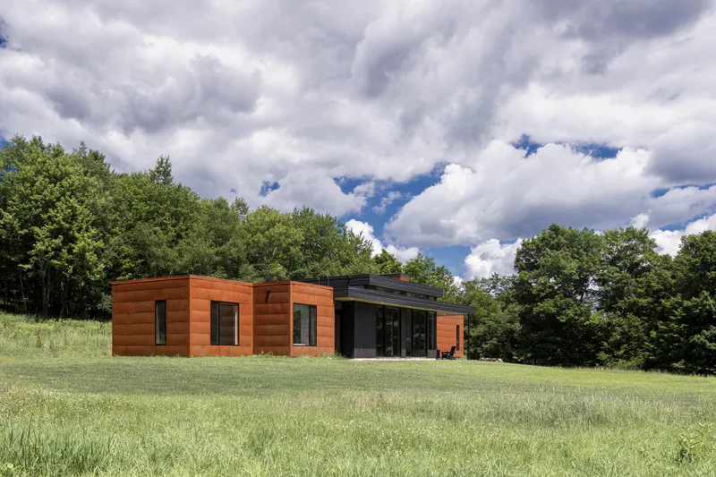 Side elevation showing timber-clad volumes and glazed living area opening to mowed lawn under dramatic clouds