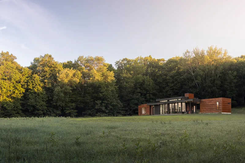 Long view across meadow of the horizontal residence with wood siding and flat roof at sunset