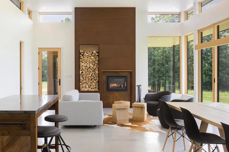 Open living and dining area with double-height fireplace wall containing stacked firewood niche and clerestory windows