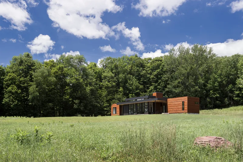 Distant view of the horizontal residence with cedar cladding and glazed center volume in a mowed meadow