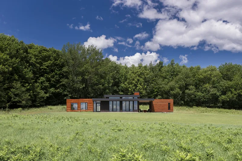Front facade showing cedar-clad wings flanking a central glazed pavilion under midday sun