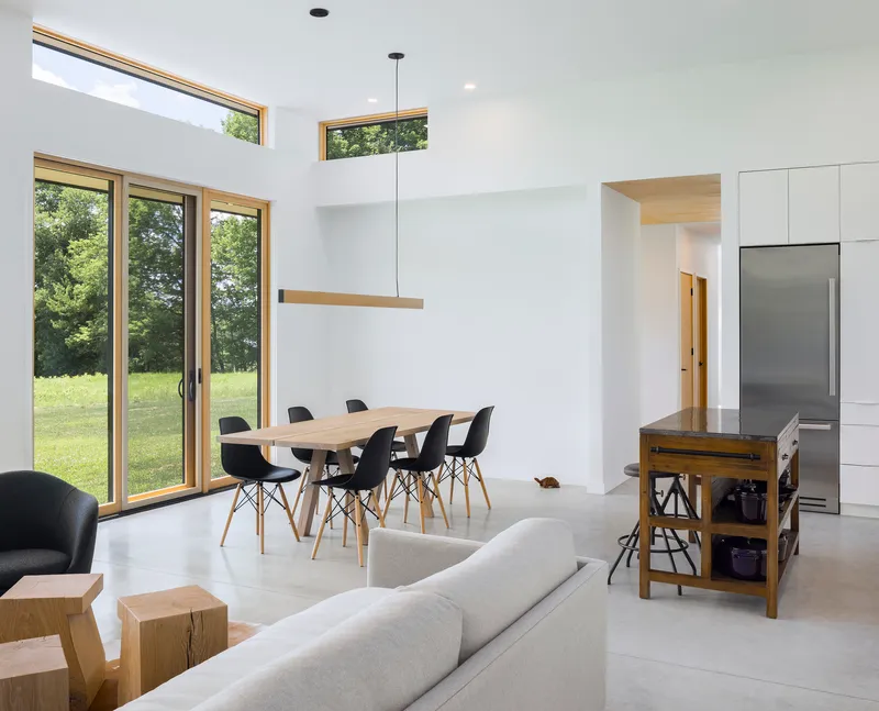 Open-plan living and dining space with clerestory windows overlooking a green meadow