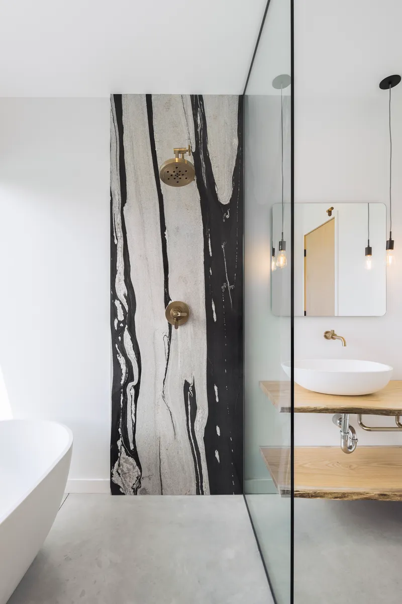 Shower wall clad in black-veined white marble slab with brass fixtures and glass partition