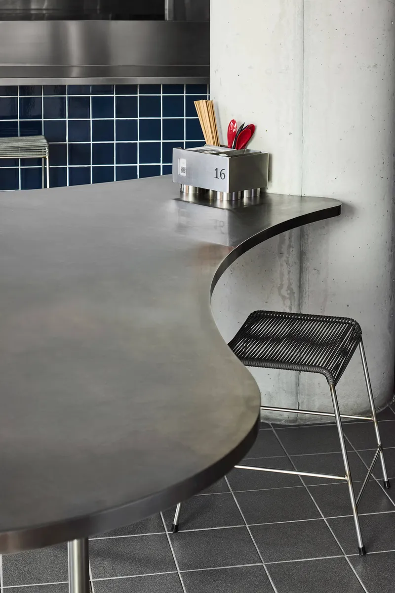 Curved metal countertop meeting concrete column with navy square tile backsplash