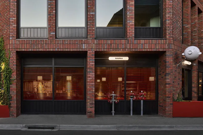 Brick facade with dark metal roller shutters and illuminated interior at dusk
