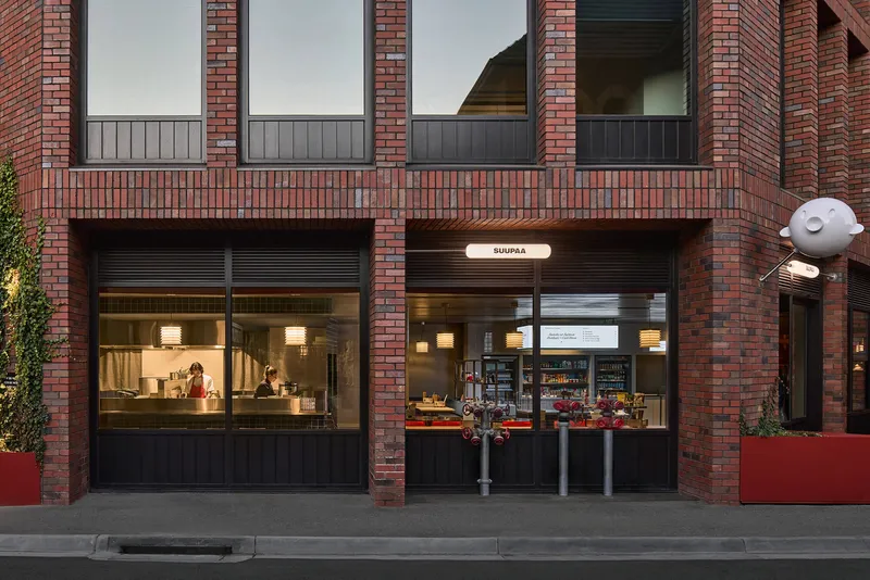 Street elevation showing dark brick facade with storefront glazing and residential balcony above at dusk