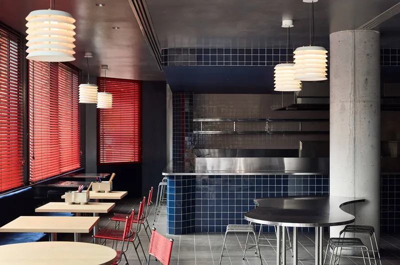 Interior dining area with navy square tile counter, red venetian blinds, and ribbed pendant lights