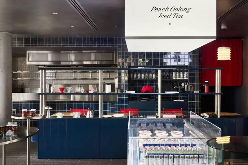 Service counter with stainless steel shelving, glass refrigerator case, and navy tile base under hanging menu sign