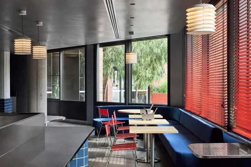 Window-side seating with blue banquette and red blinds looking onto green planting outside