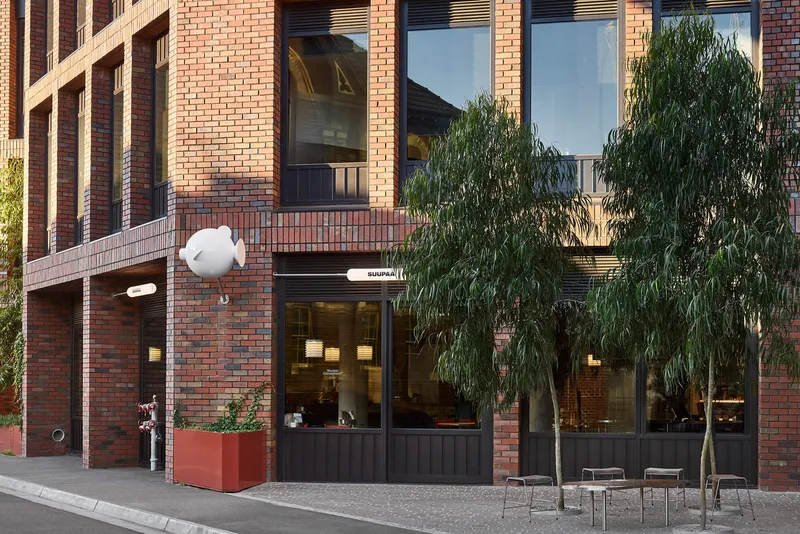 Street view of the red brick facade with ground-floor cafe storefront and a weeping willow