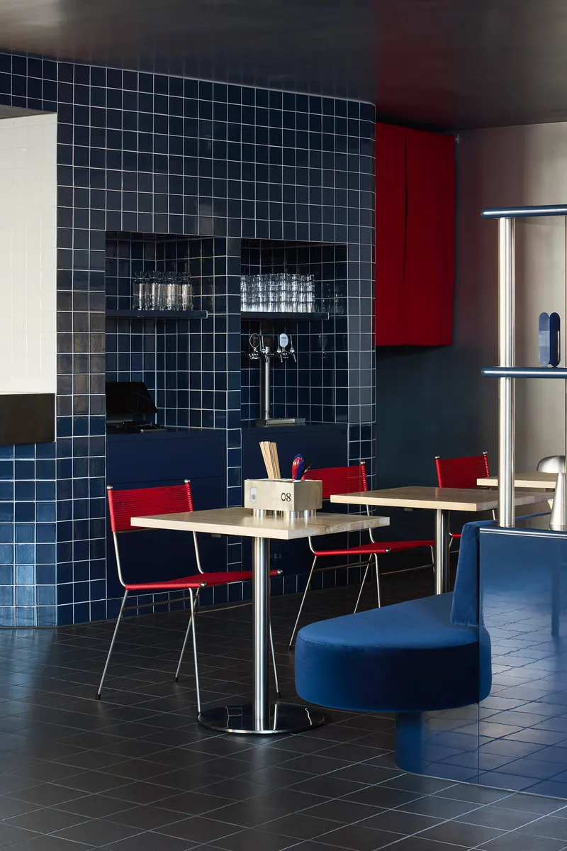 Navy tiled wall with recessed shelving niche beside tables and red cabinet panels