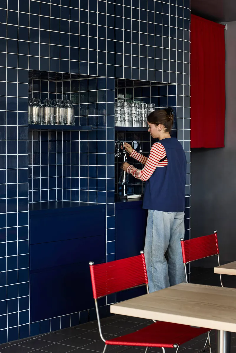 Person in striped shirt preparing a beverage at the chrome tap set into the tiled niche