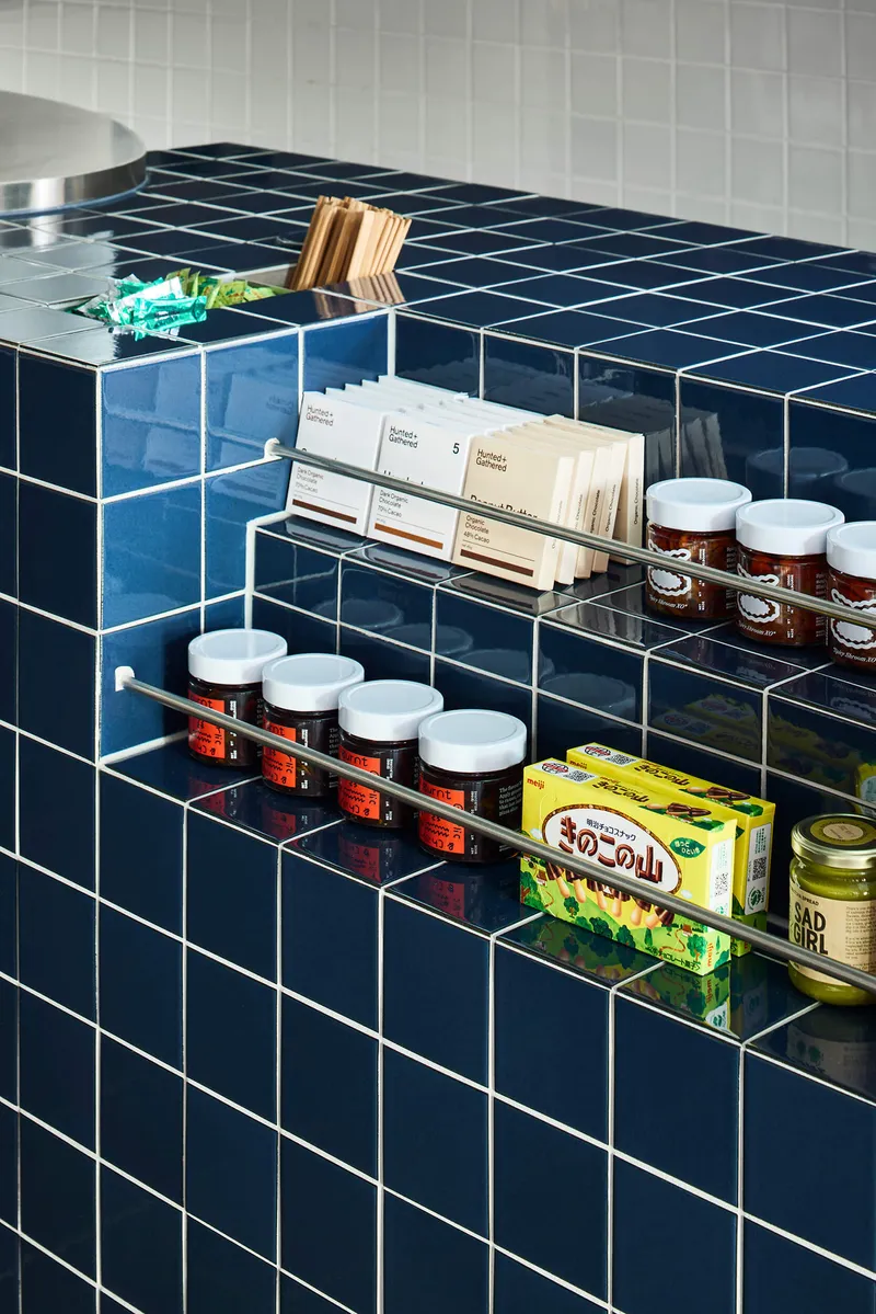 Clear acrylic shelves mounted on blue tile wall holding packaged goods and glass jars with labels