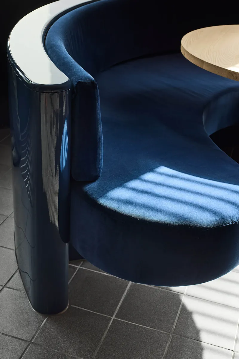 Navy velvet curved seating with chrome tubular legs and striped sunlight on grey tile floor
