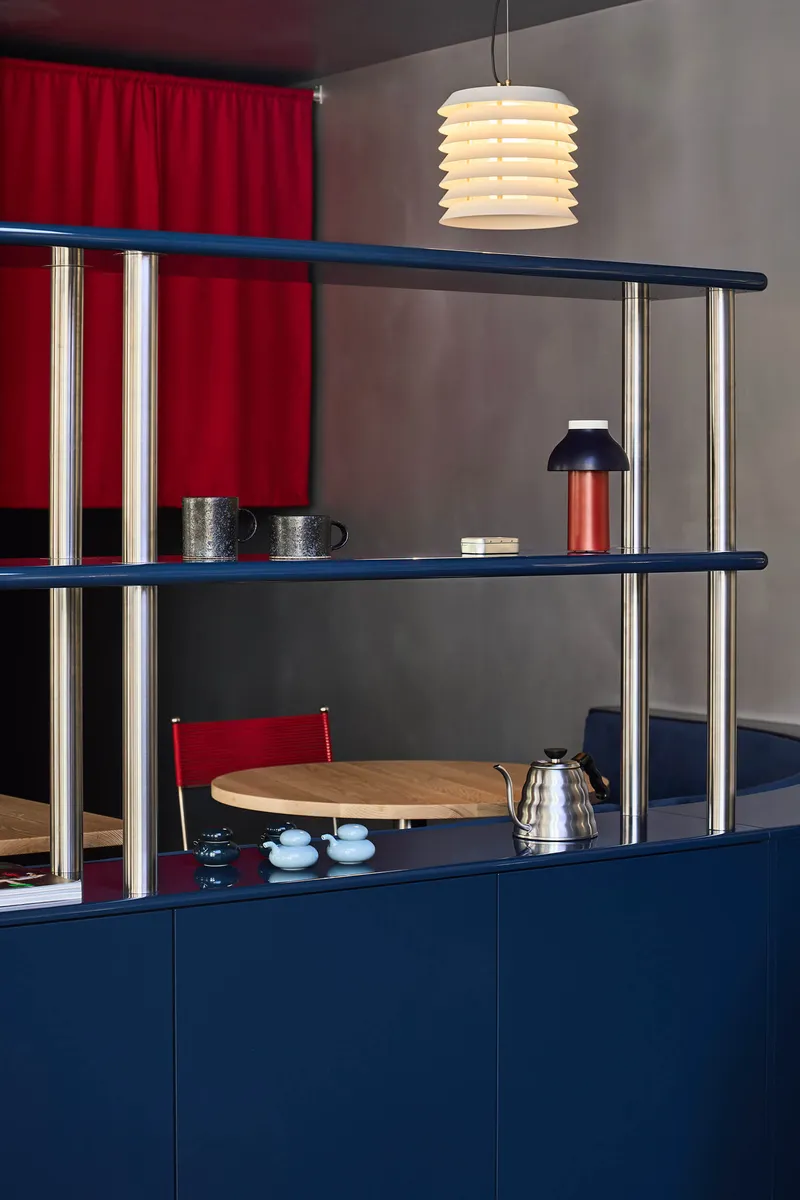Chrome tube shelving with navy blue surfaces and red curtain behind pendant lamp