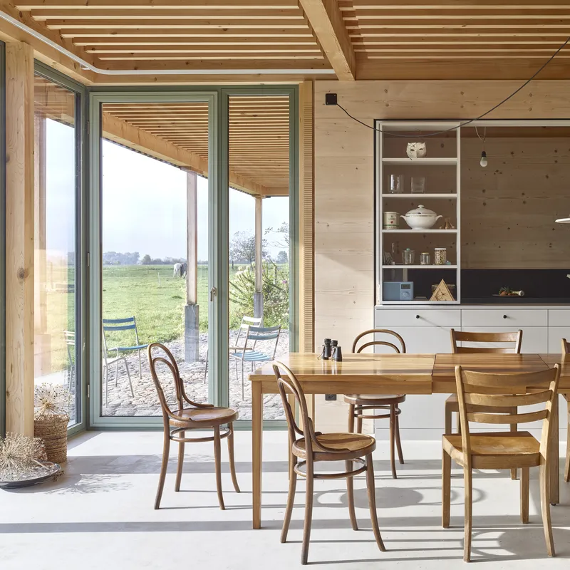 Dining area with timber ceiling beams and sliding glass doors opening to a covered terrace in daylight