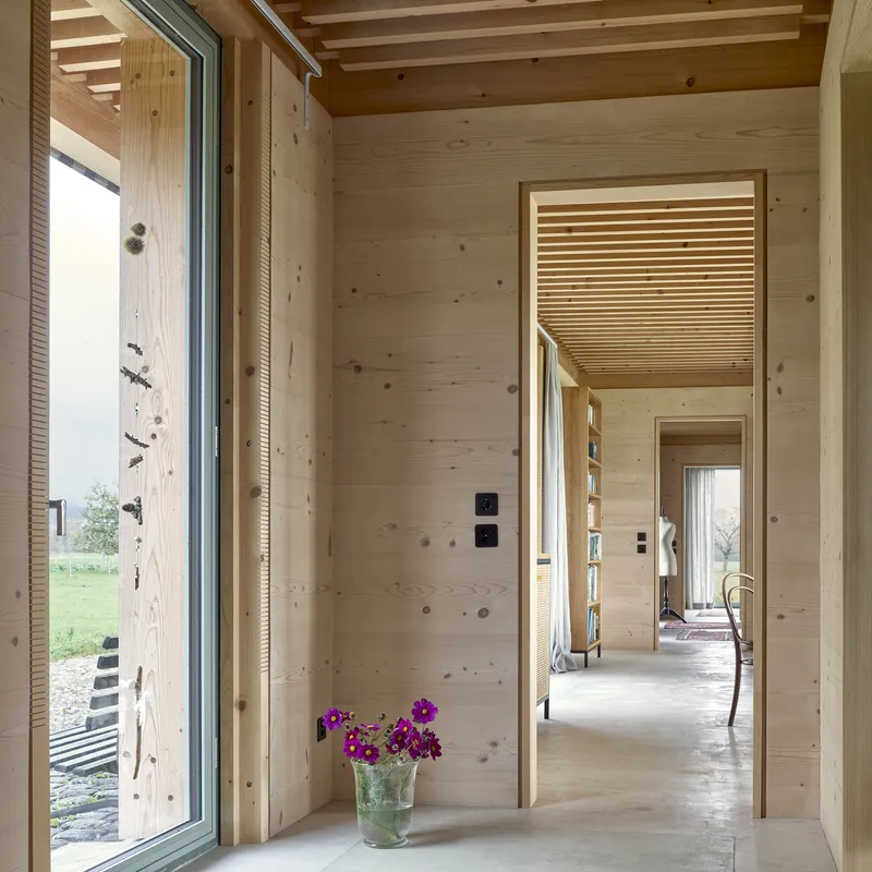 View through aligned doorways showing timber-clad walls, slatted ceiling inserts, and purple flowers on the floor