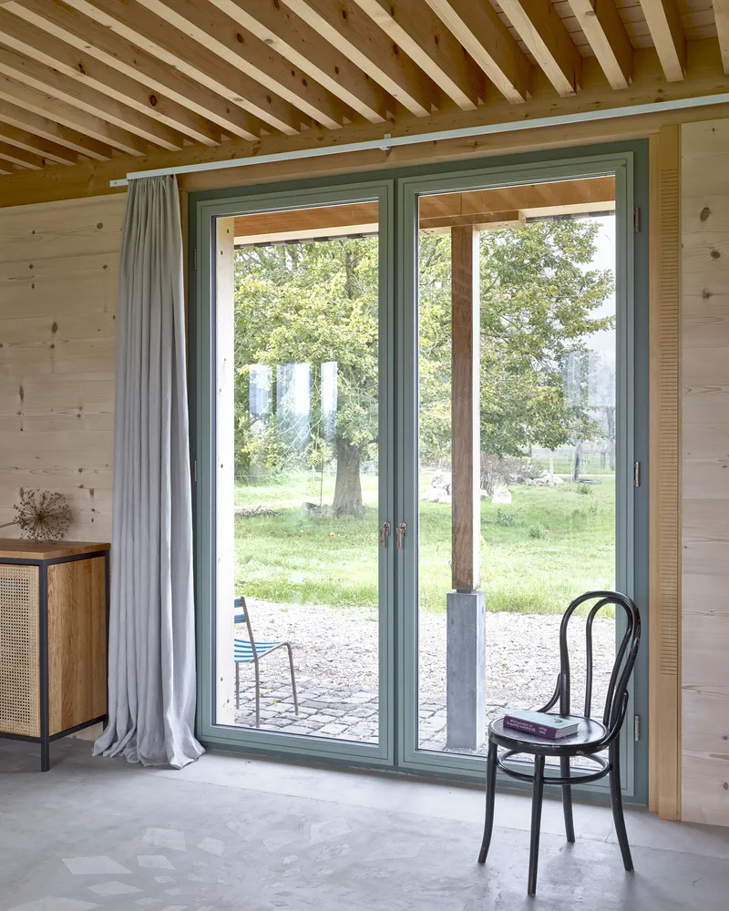 Glazed door opening to gravel terrace with a bentwood chair beneath an exposed timber beam ceiling