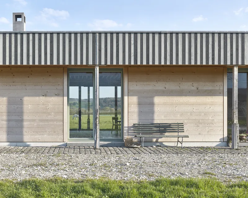 Facade detail showing vertical striped metal cladding above concrete walls with glazed doors and steel columns