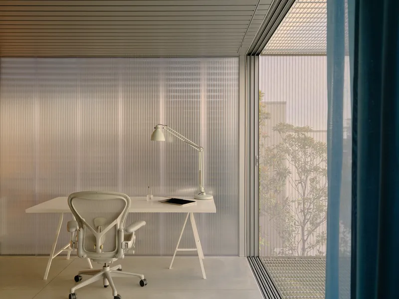 Home office with trestle desk and fluted glass wall opening to balcony at dusk