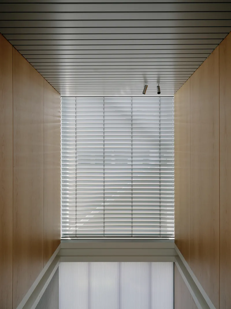 Wood-lined corridor with slatted metal ceiling and horizontal louvered window at end