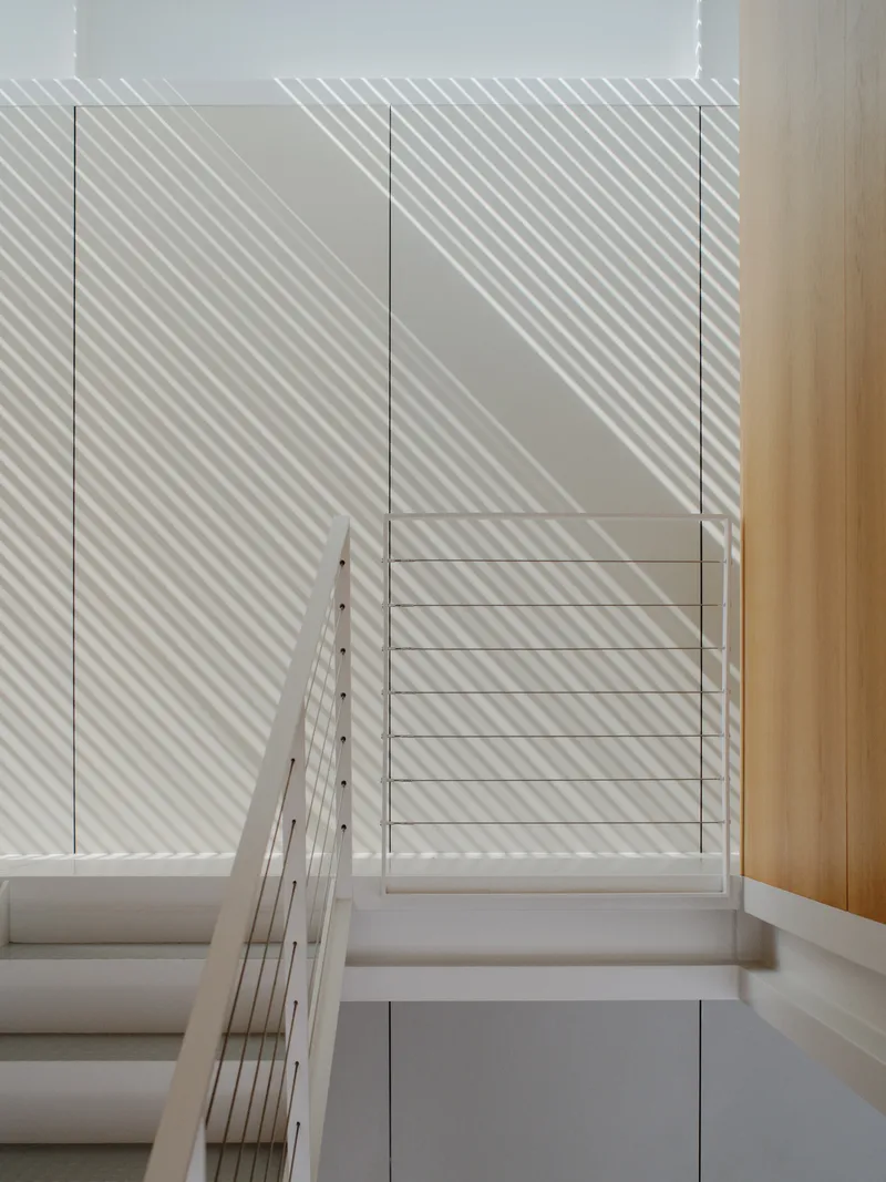 White stairwell with glass balustrade and diagonal shadow patterns from exterior louvers
