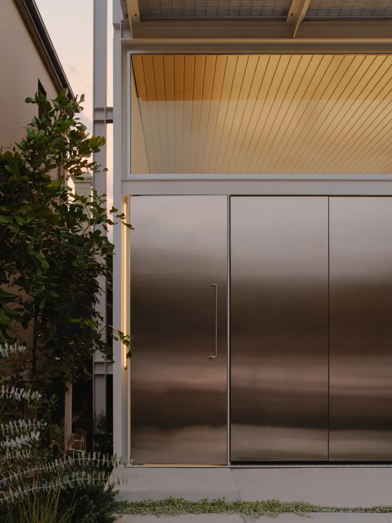 Entry detail showing brushed metal doors beneath wood-paneled soffit at dusk