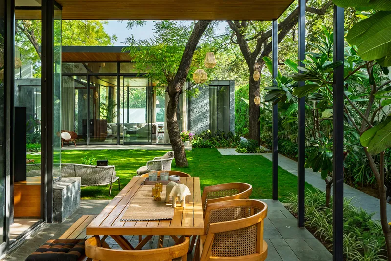 Covered terrace with dining table and woven chairs overlooking the courtyard lawn and tree