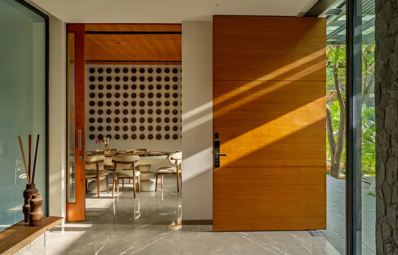 Timber pivot door in afternoon sunlight leading to the dining room with perforated wall panel