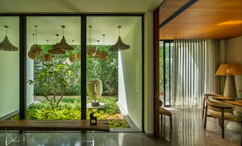 Bedroom desk with woven pendant lamps suspended above a vertical garden beyond the glass wall