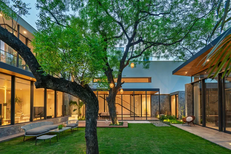 Central courtyard with preserved tree between glass-walled pavilions and stone volumes under an overcast sky