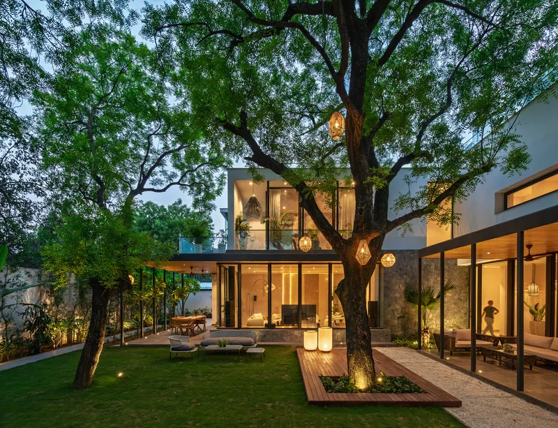 Evening view of the courtyard showing the tree-wrapped pavilions with illuminated interiors and pendant lighting
