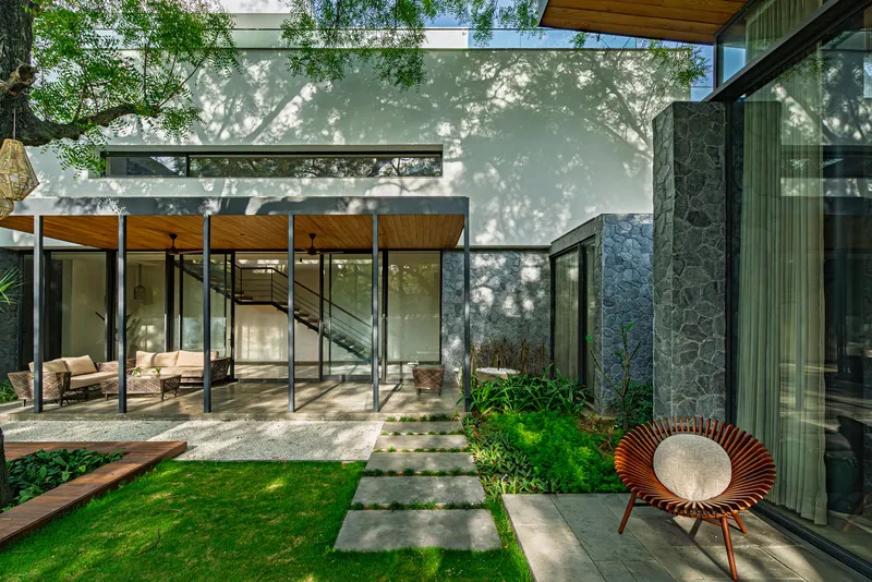 View across the courtyard lawn showing glass pavilions and concrete stepping stones with tree shadows on white walls