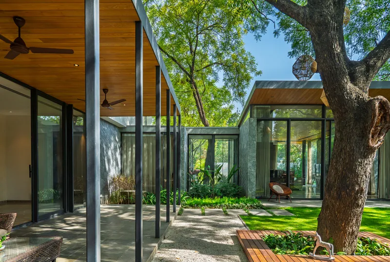 Multiple glass-walled pavilions with timber soffits arranged around a central garden with mature trees