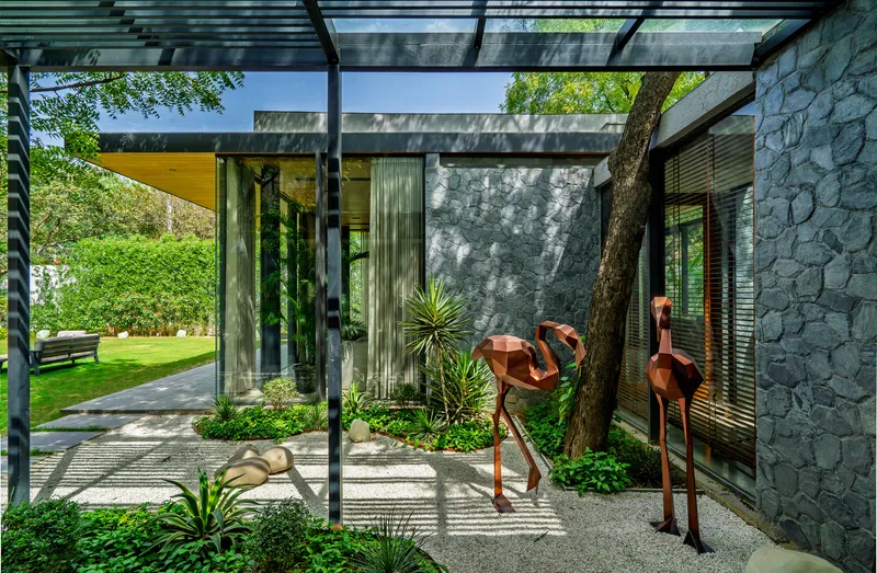 Steel pergola framing a view of the tree trunk wrapped in stone wall with gravel and planted ground cover