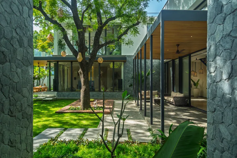 Courtyard with stone-clad volumes, glazed walkways, and an existing tree preserved in the lawn
