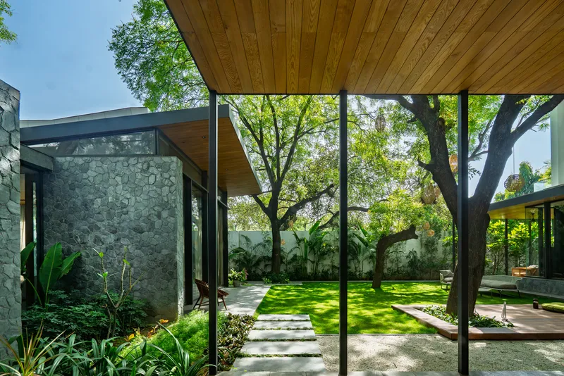 Covered passage with timber soffit and steel columns framing views of the garden and stone walls