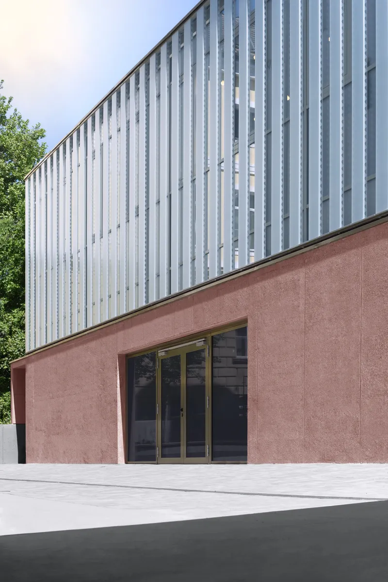 Two-story volume with pink stucco base and vertical white metal cladding beside green trees