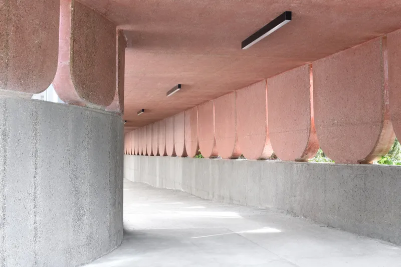 Covered walkway with pink scalloped ceiling and gray concrete benches allowing glimpses of greenery