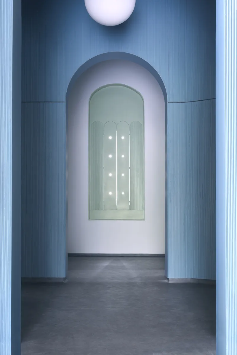 Arched doorway framing a niche with illuminated recess under a ceiling-mounted sphere in blue light
