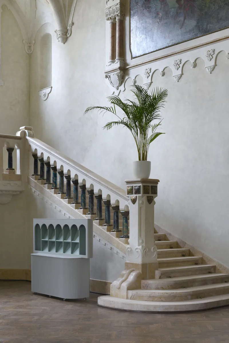 Curved stone staircase with dark metal balusters and potted palm at the newel post