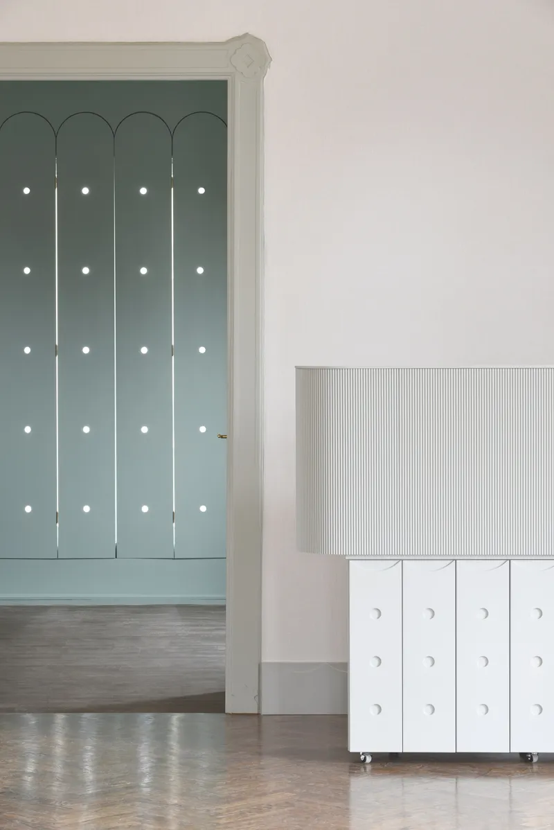 Arched doorway with green panels and white circular pulls beside a wheeled cabinet with ribbed front