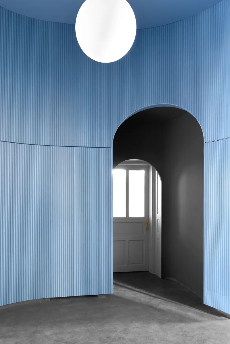 Blue paneled room with black arched portal leading to a white door and hanging globe light