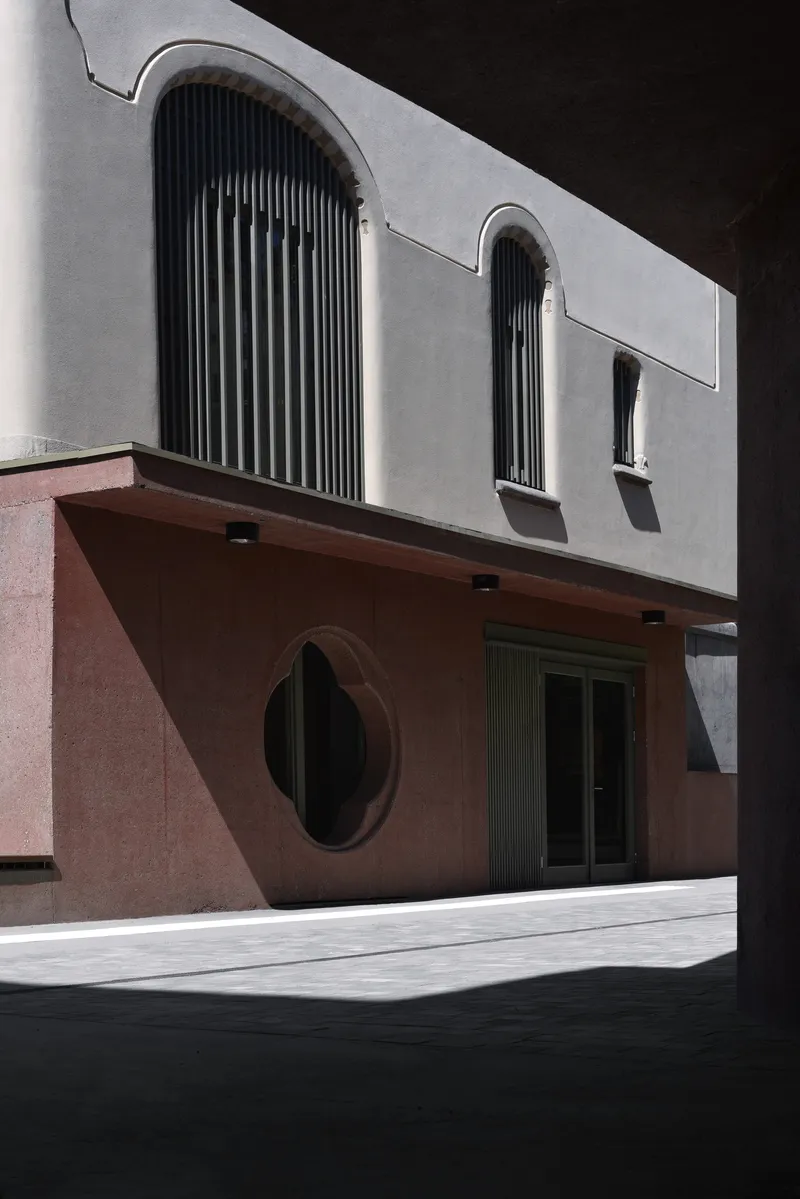 Street view of pink and white stucco facade with oval window and cantilever overhang in harsh sunlight