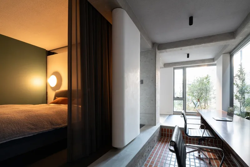 Bedroom alcove with circular wall sconces separated from workspace by white column and glazed terrace