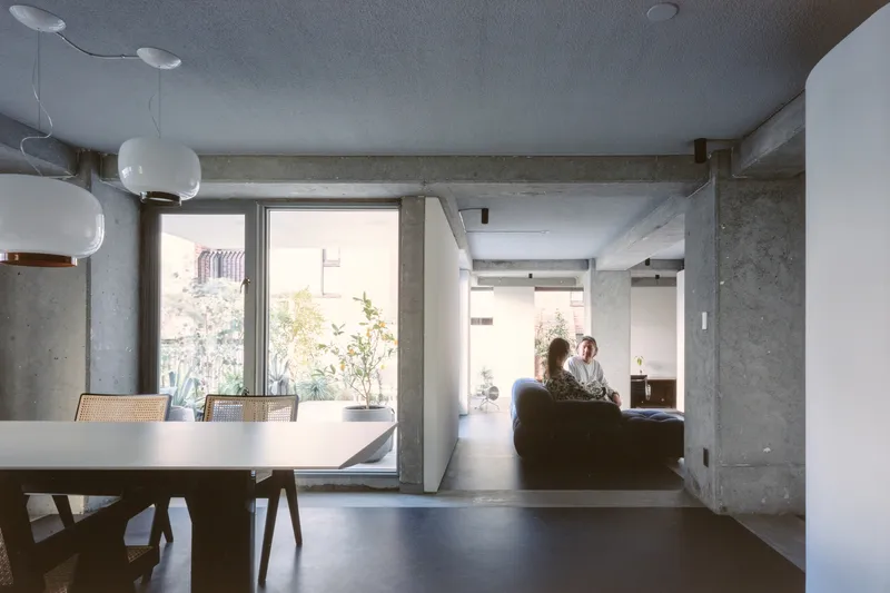 Living and dining zones divided by white partition with two residents seated on sofa