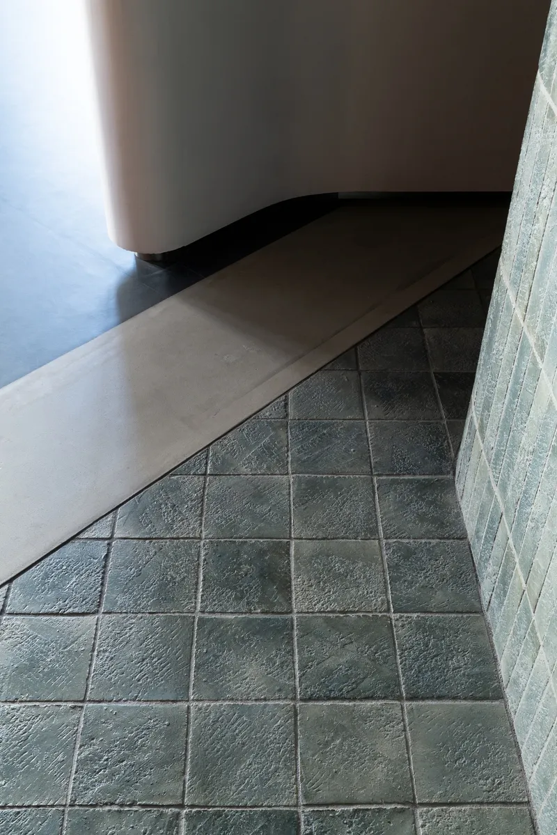 Curved white bench meeting dark tile floor along textured concrete block wall
