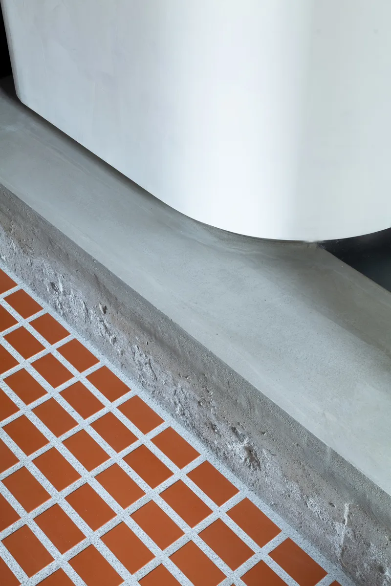 Detail of cast concrete ledge meeting white curved wall above orange tile floor with white grout