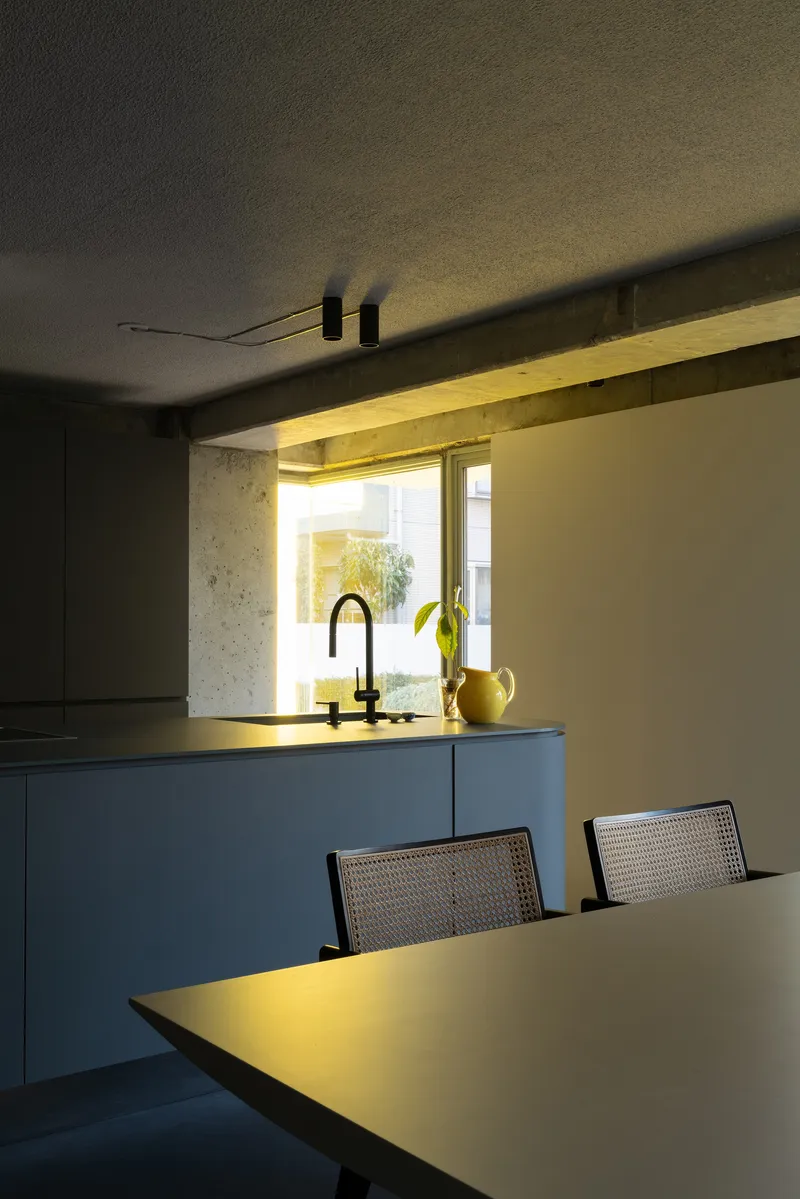 Concrete window niche with integrated yellow lighting framing kitchen sink and yellow pitcher at dusk