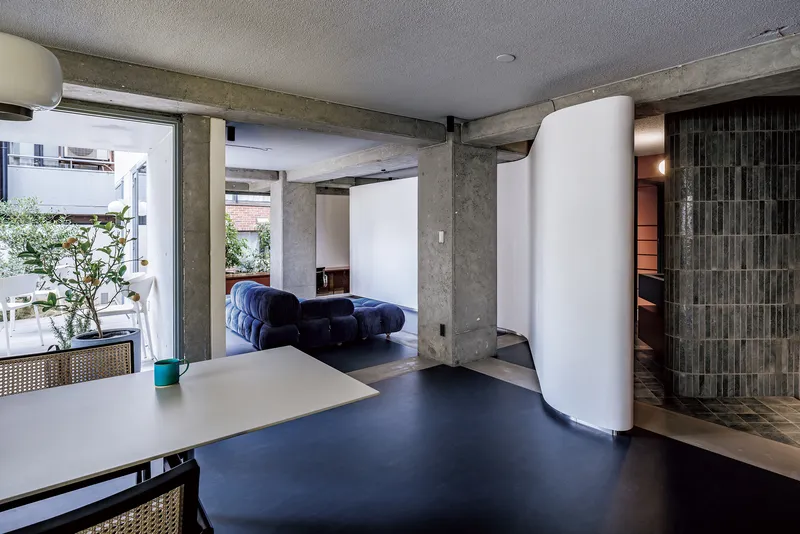 Open living area with exposed concrete beams and curved white partition separating spaces with terrace beyond